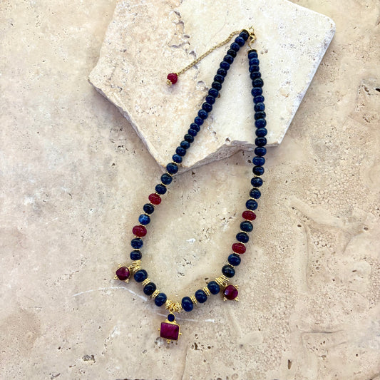 Collier Sophia composé de perles de sodalite bleu profond, de quartz framboise facetté et d’intercalaires plaqués or, présenté à plat sur une surface en pierre claire.