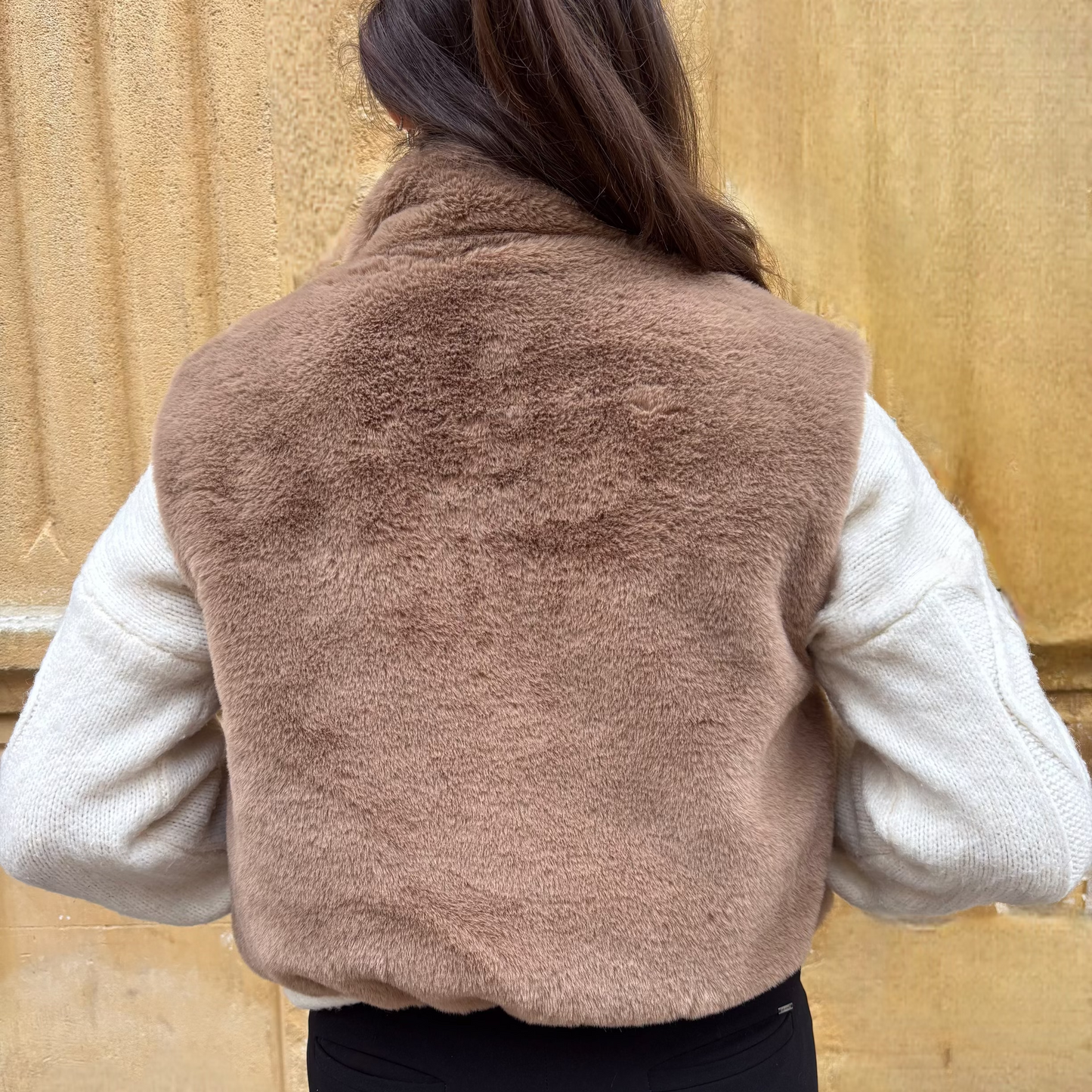 Gilet sans manches taupe en fausse fourrure, porté sur un pull torsadé écru, vue de dos