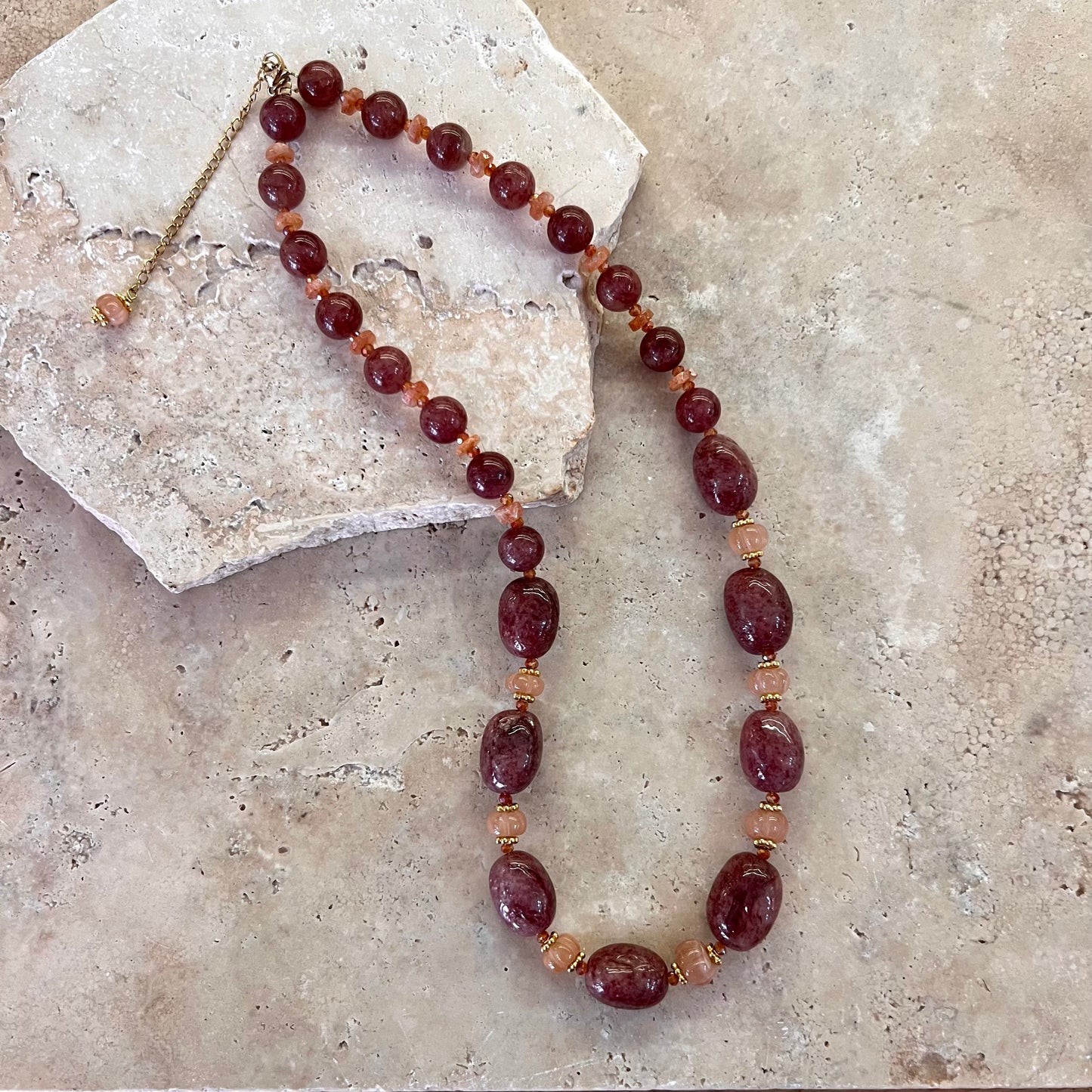Collier Gaby composé de perles de quartz framboise et de pierre de lune pêche, monté avec des intercalaires dorés sur un fond minéral clair.