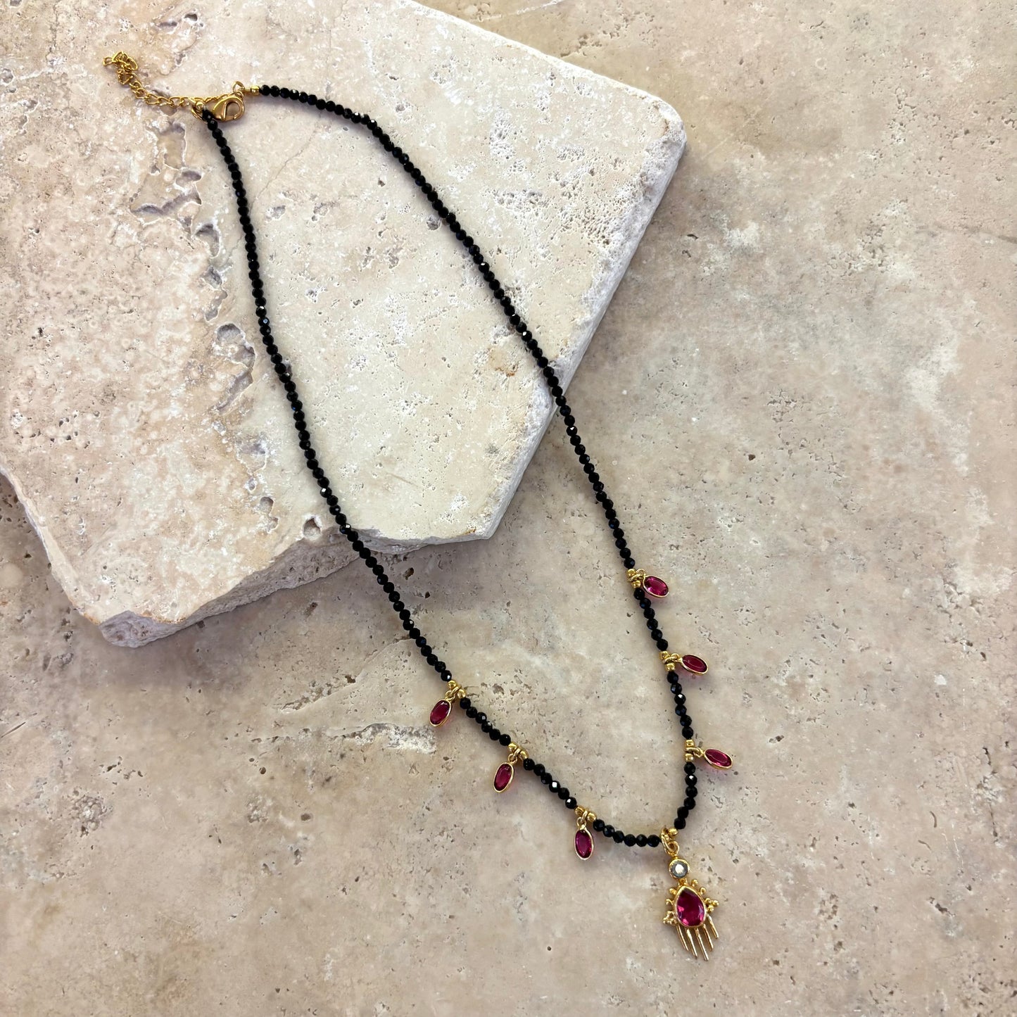 Collier Birdy noir composé de perles d’onyx noir et de pampilles en quartz framboise serties or, présenté dans son intégralité sur une surface en pierre claire.