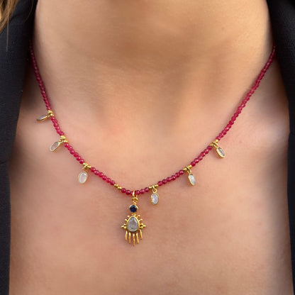 Collier Birdy Mademoiselle Azalée à Agen, porté, en perles rubis avec gouttes de pierre de lune et pendentif central doré serti d’une pierre nacrée