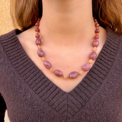 Collier Gaby porté, composé de perles de quartz framboise et de pierre de lune pêche avec intercalaires dorés, présenté autour du cou d’une femme portant un pull col V marron.
