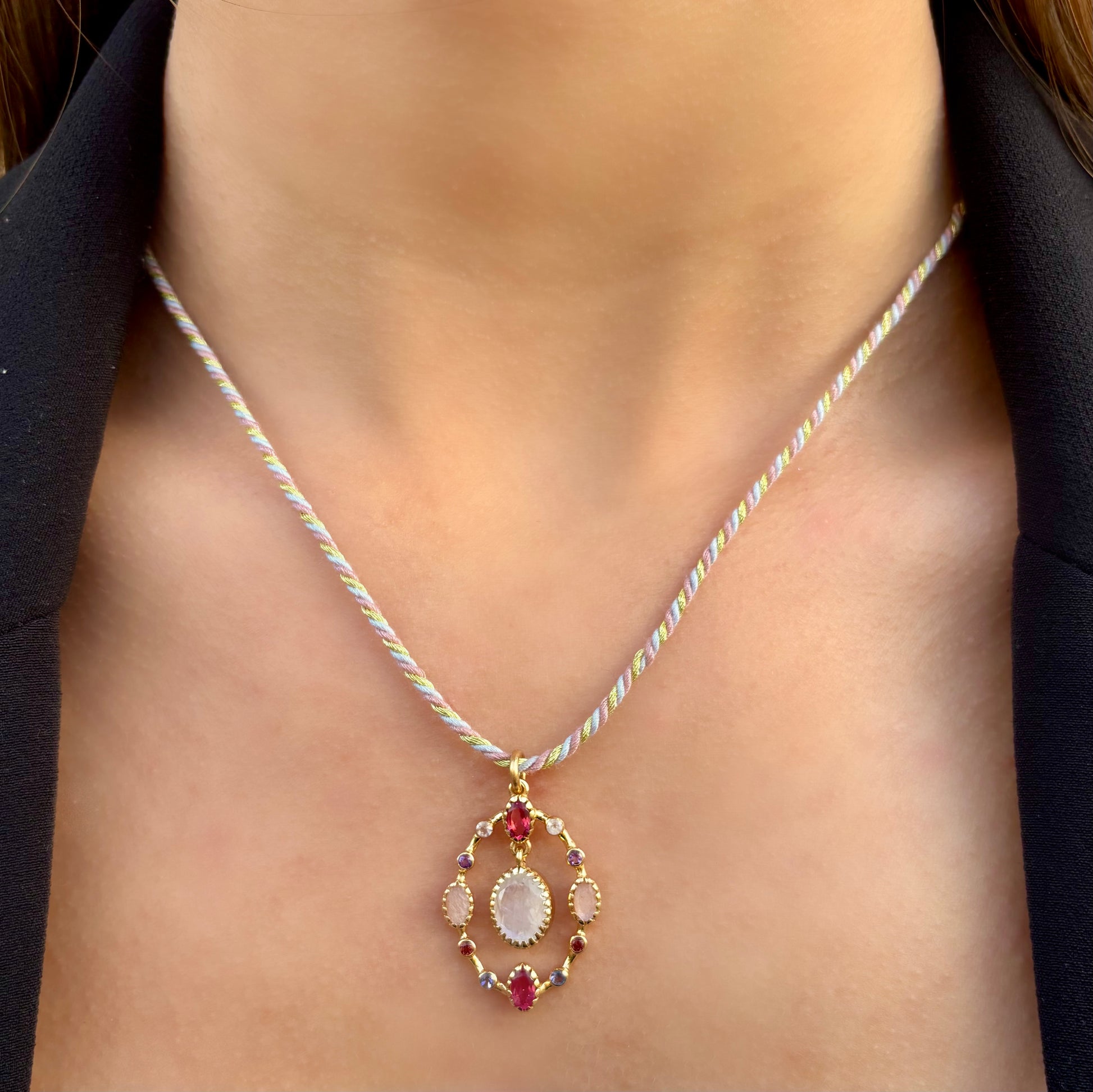 Collier Goa porté, composé d’un pendentif en pierre de lune sculptée aux reflets nacrés, entourée de quartz rose et de quartz framboise, monté sur un cordon torsadé pastel avec finitions dorées.