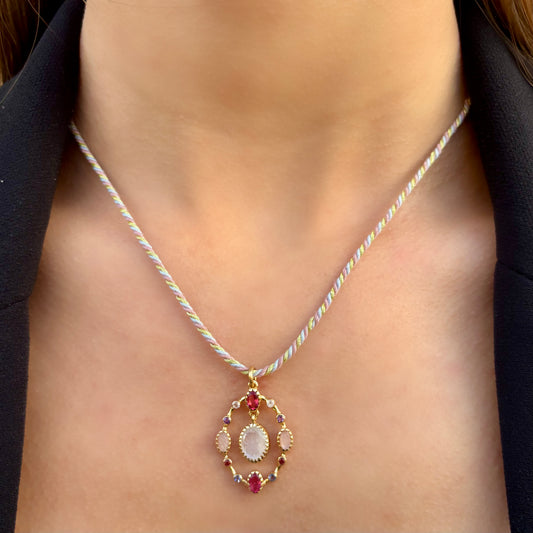 Collier Goa porté, composé d’un pendentif en pierre de lune sculptée aux reflets nacrés, entourée de quartz rose et de quartz framboise, monté sur un cordon torsadé pastel avec finitions dorées.