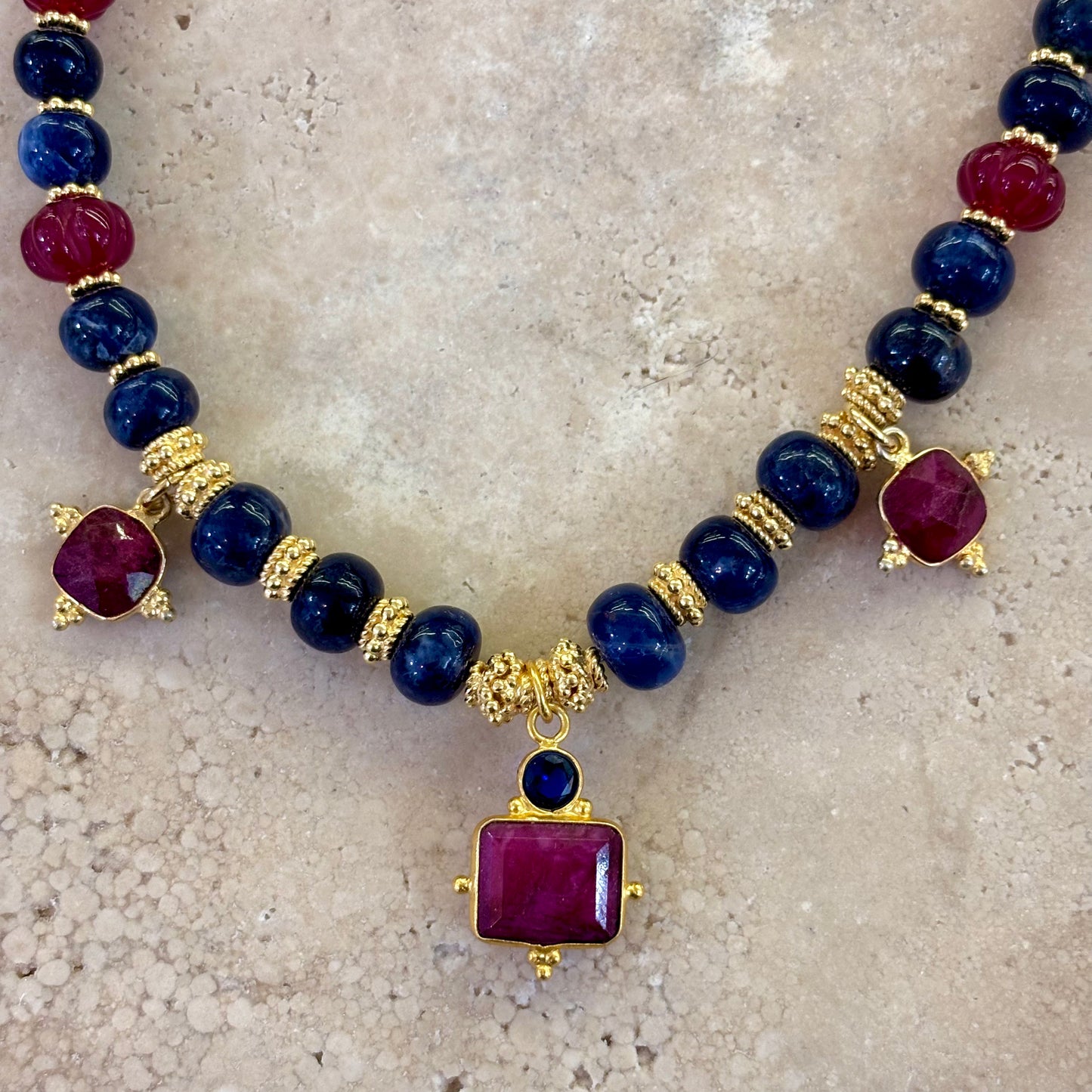 Détail du collier Sophia composé de perles de sodalite bleu profond, de quartz framboise facetté et d’intercalaires plaqués or, avec un pendentif carré framboise monté sur dorure.