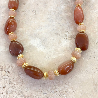 Détail d’un collier en pierre de lune pêche, composé de galets polis et de petites perles sculptées en forme de melons, monté avec des intercalaires plaqués or.