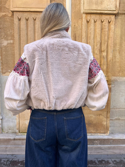 Gilet sans manches beige en fausse fourrure, porté ouvert sur une blouse imprimée rouge et un jean taille haute, vue de dos