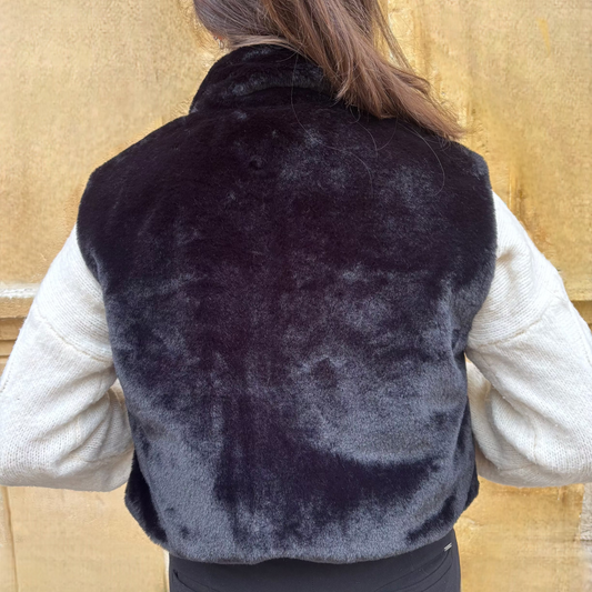 Gilet sans manches noir en fausse fourrure, porté sur un pull torsadé écru, vue de dos