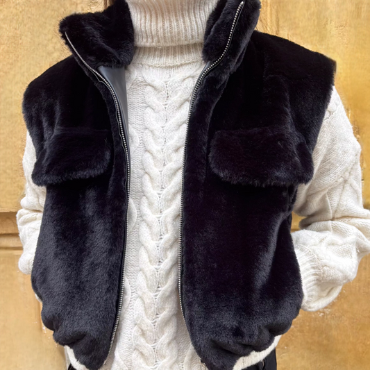 Gilet sans manches noir en fausse fourrure, porté sur un pull torsadé écru, vue de face