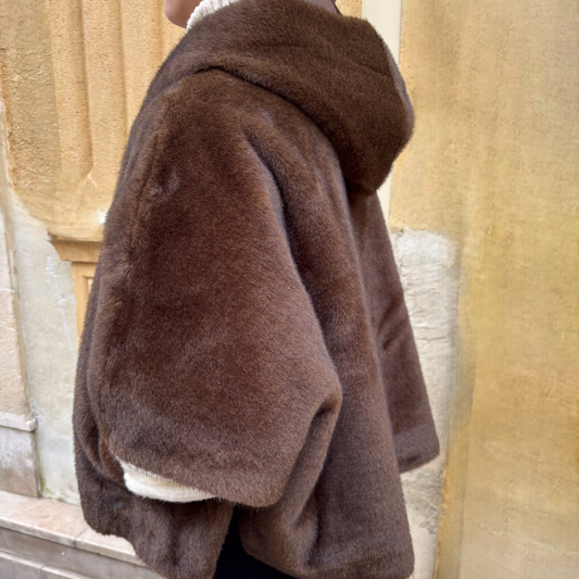 Cape marron en fausse fourrure portée de face, avec fermeture zippée et col montant, superposée à un pull torsadé écru