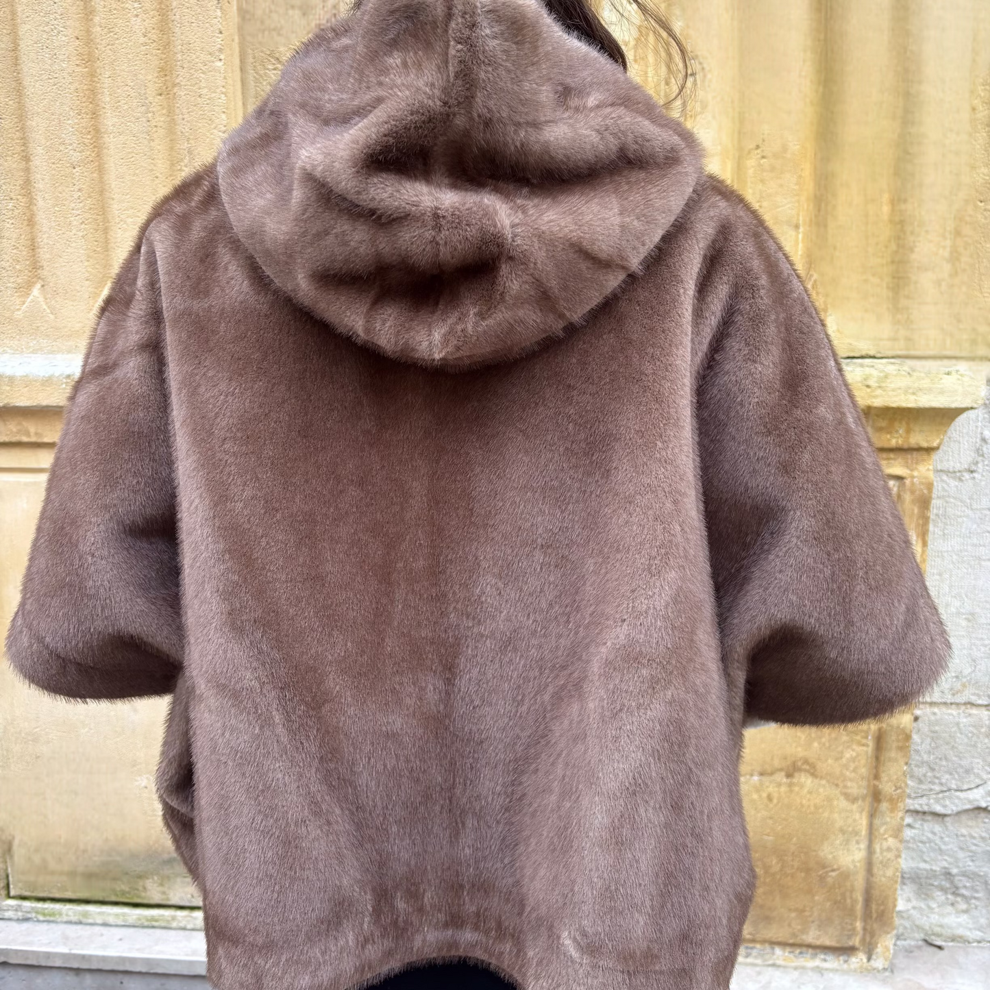 Cape taupe en fausse fourrure avec capuche, portée de face, fermeture zippée et manches courtes, superposée à un pull écru