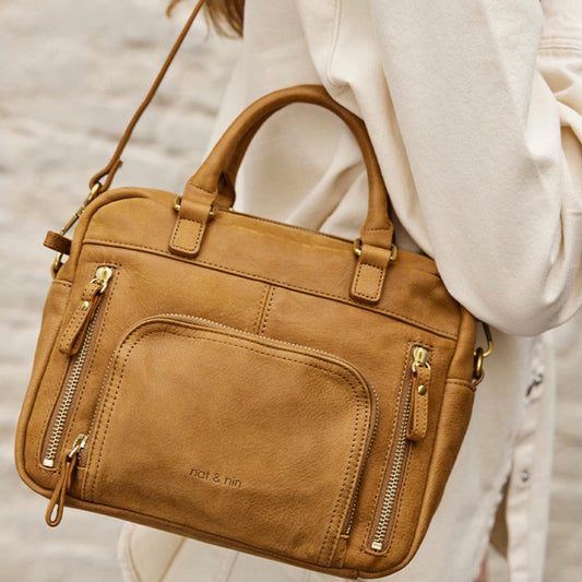 Femme portant le sac Mini Macy couleur épice de Nat & Nin à l’épaule, petit sac en cuir camel avec poches zippées et anses rigides.