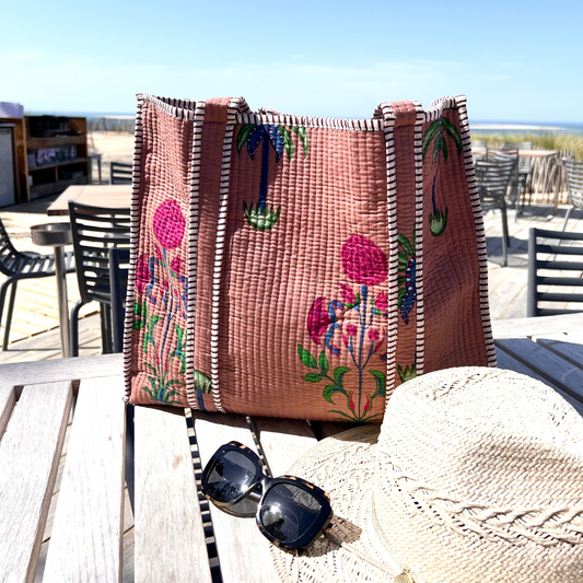 Sac cabas Palmito en coton matelassé, création Mademoiselle Azalée à Agen, posé sur une table en terrasse avec chapeau de paille et lunettes de soleil, face à une vue de plage