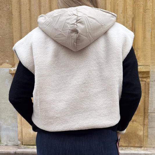 Gilet sans manches écru réversible, porté ouvert sur un pull noir et une chemise blanche, vue de dos