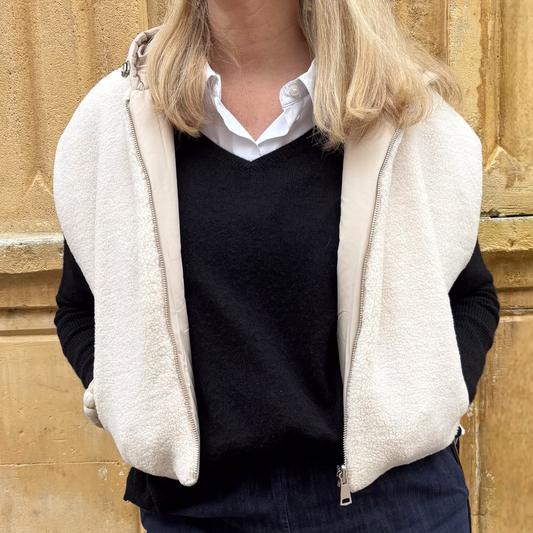 Gilet sans manches écru réversible, porté ouvert sur un pull noir et une chemise blanche, vue de face